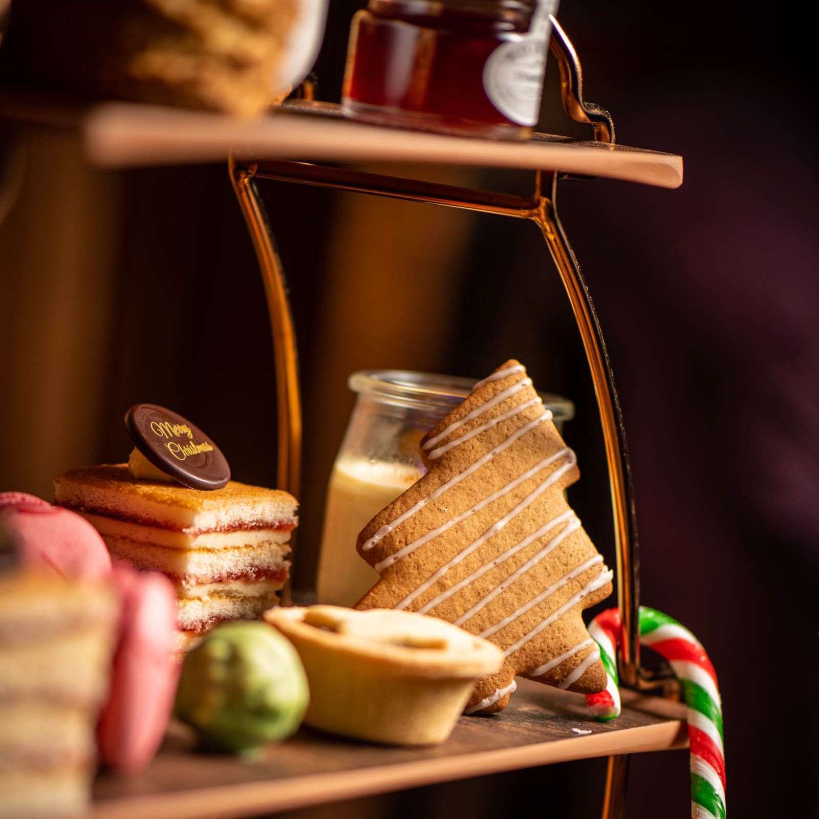 Festive afternoon tea tray with Christmas-themed treats including a tree-shaped cookie, candy cane, layered cake, and mince pie.