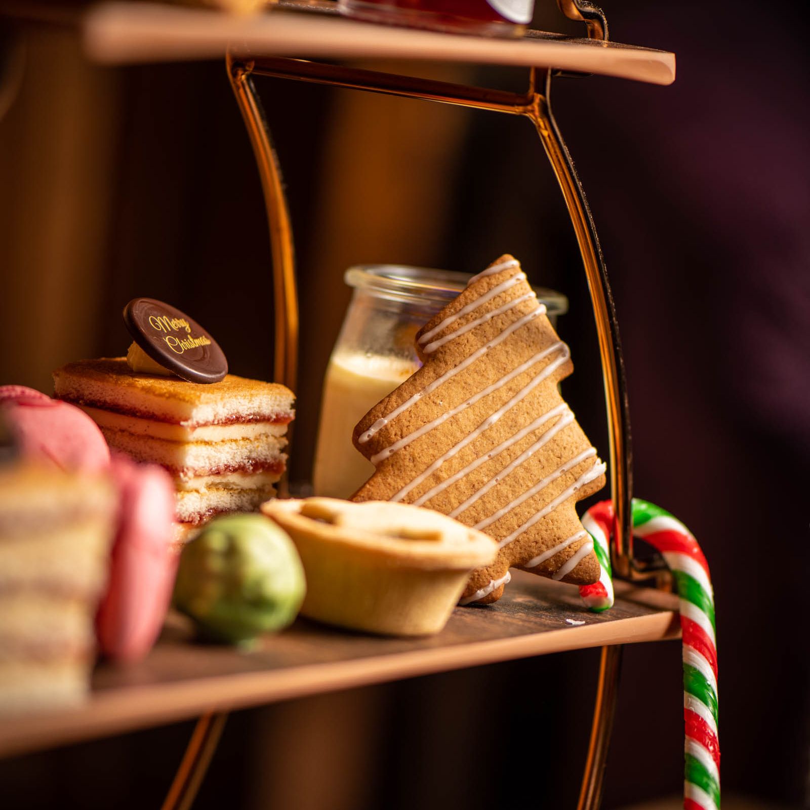Festive afternoon tea tray with Christmas-themed treats including a tree-shaped cookie, candy cane, layered cake, and mince pie.