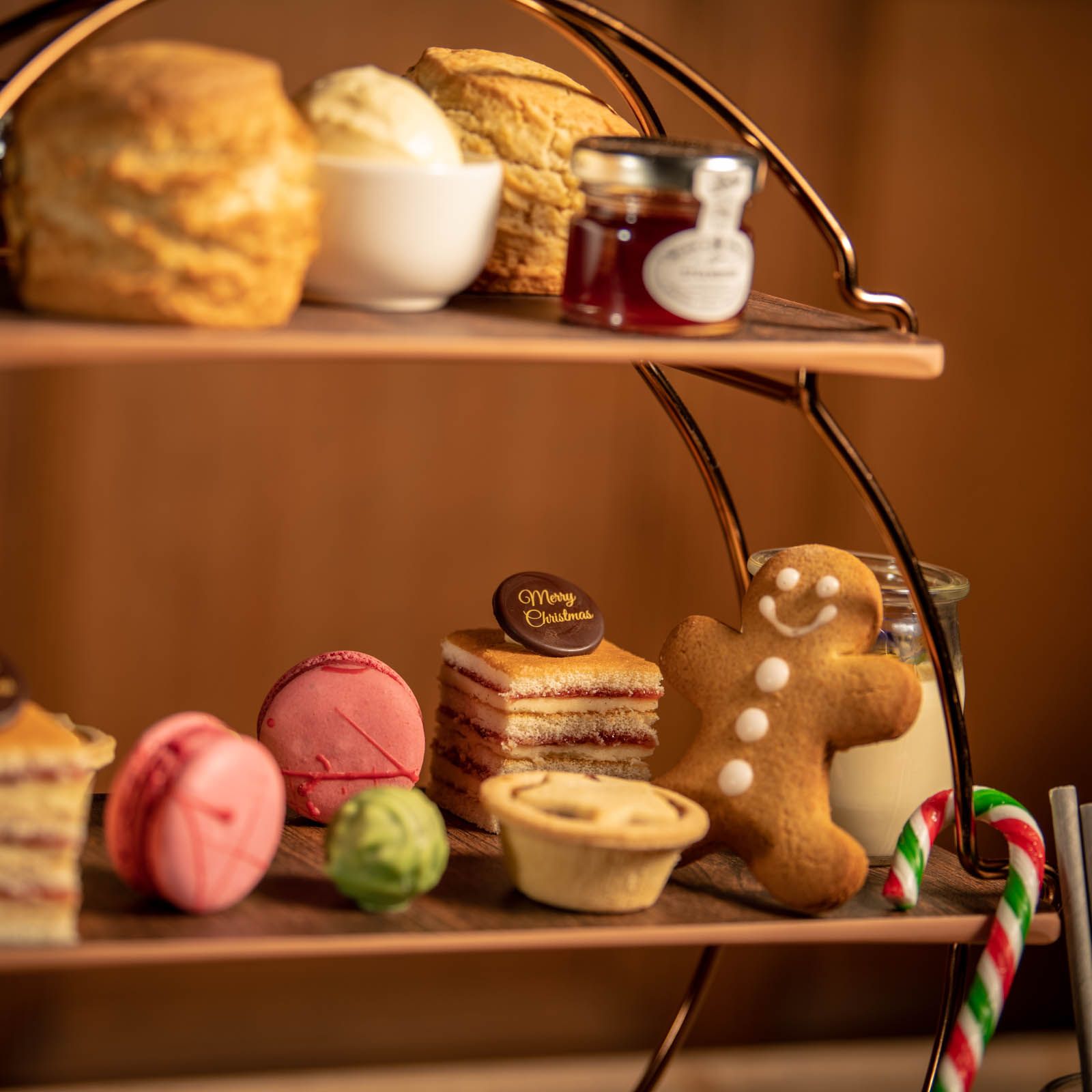 Festive afternoon tea stand with scones, clotted cream, jam, macarons, cakes, a gingerbread man, and candy canes.