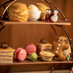 Festive afternoon tea stand with scones, clotted cream, jam, macarons, cakes, a gingerbread man, and candy canes.