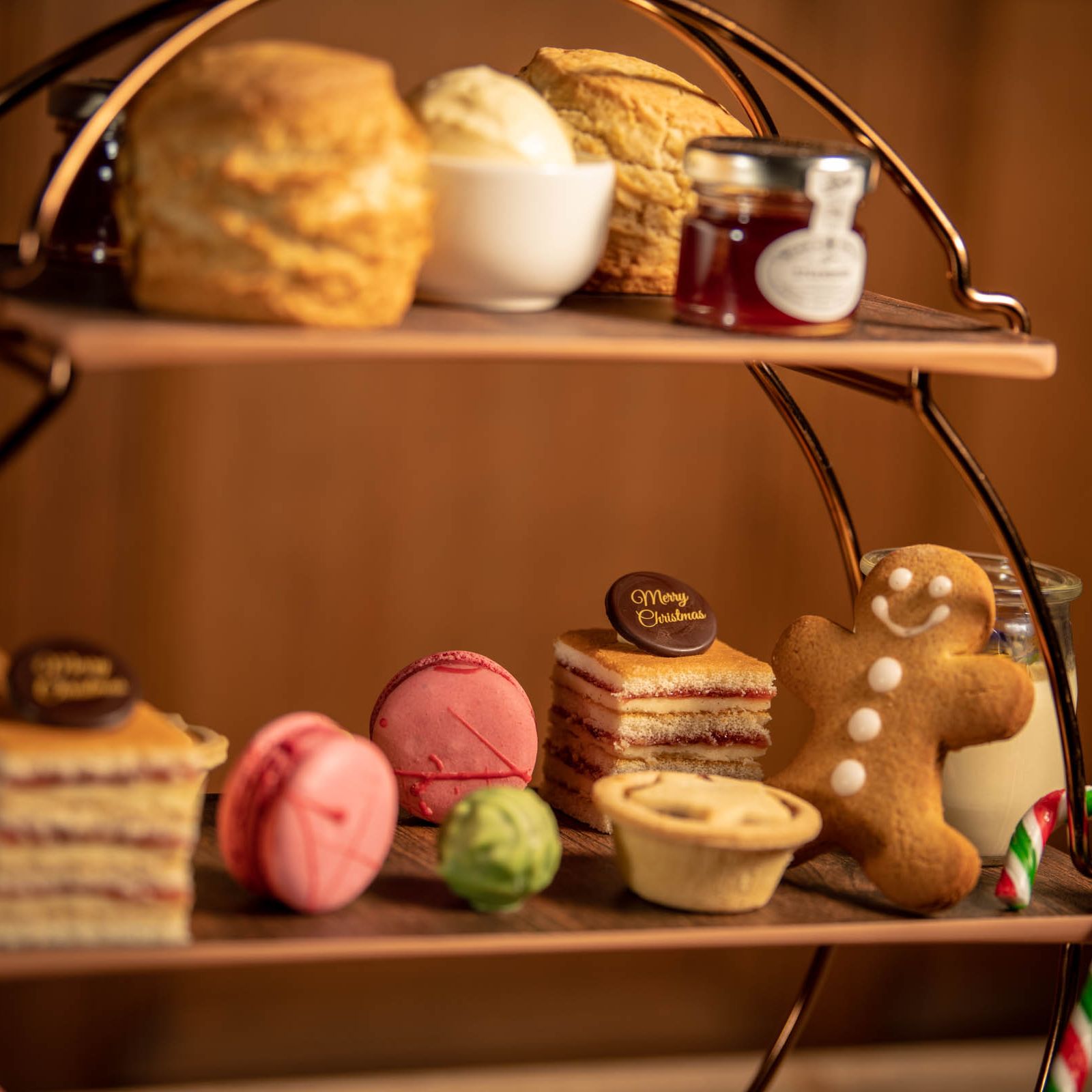 Festive afternoon tea stand with scones, clotted cream, jam, macarons, cakes, a gingerbread man, and candy canes.