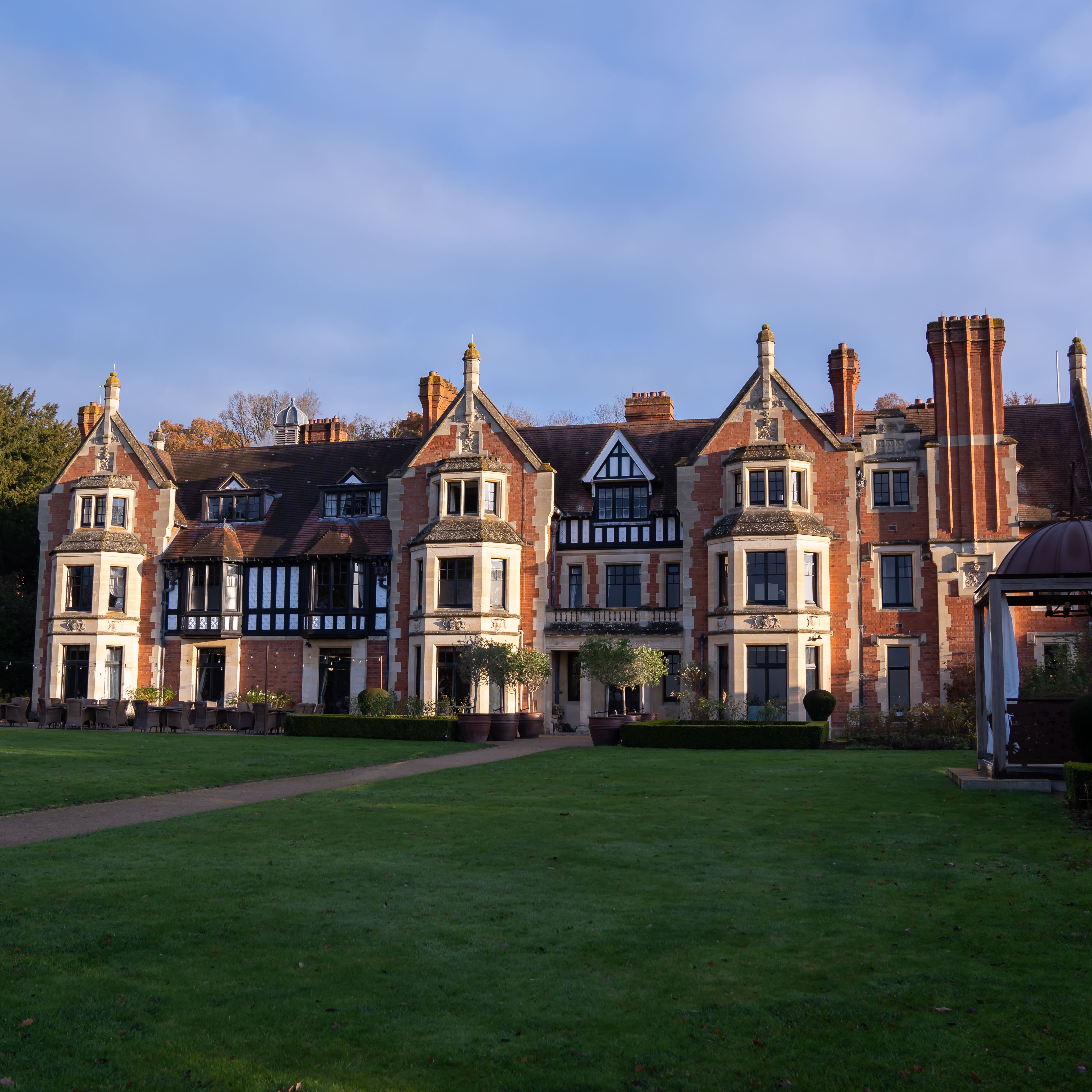 A large, historic manor house with multiple chimneys, brick and stone façade, and a well-kept lawn in front.