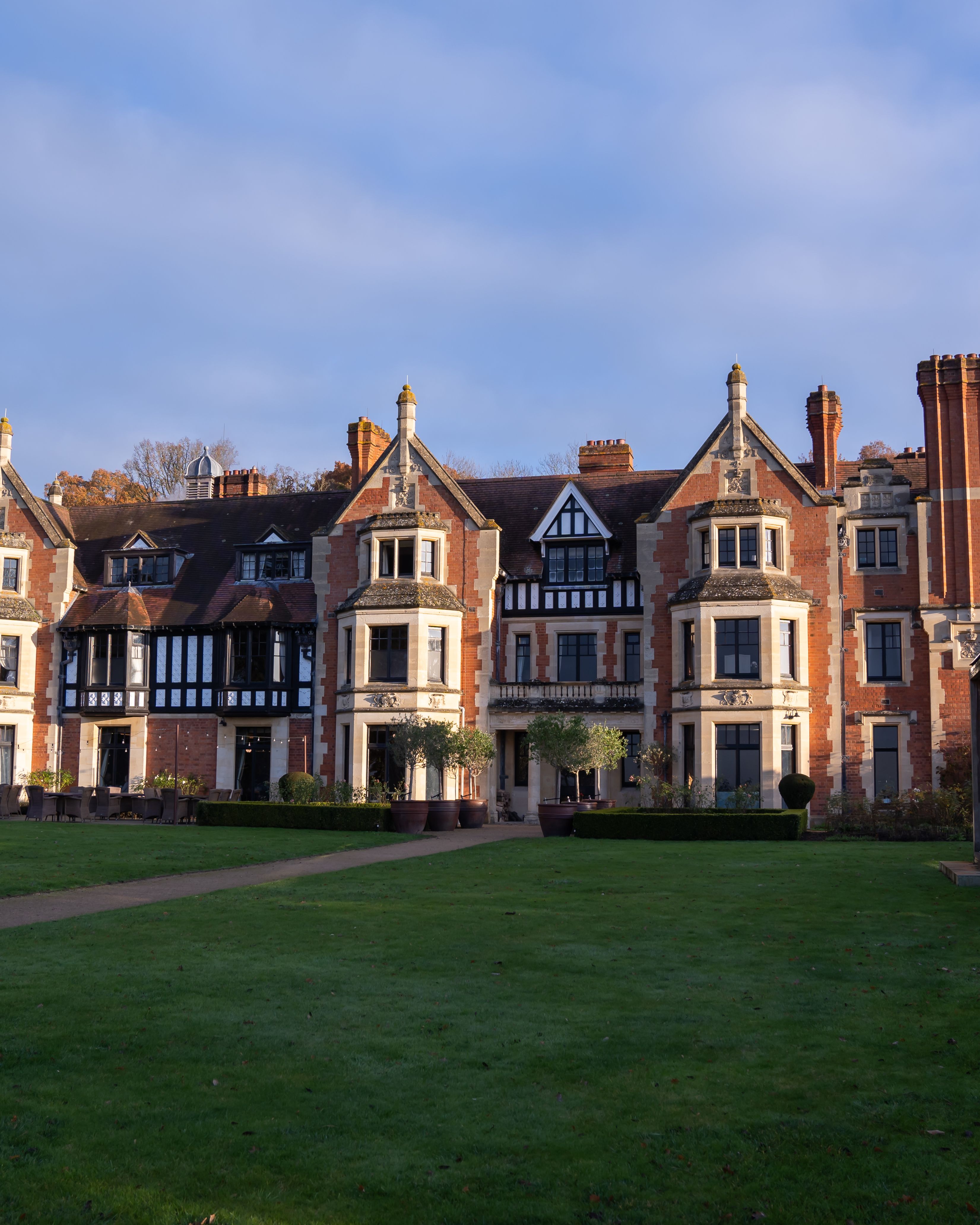 A large, historic manor house with multiple chimneys, brick and stone façade, and a well-kept lawn in front.
