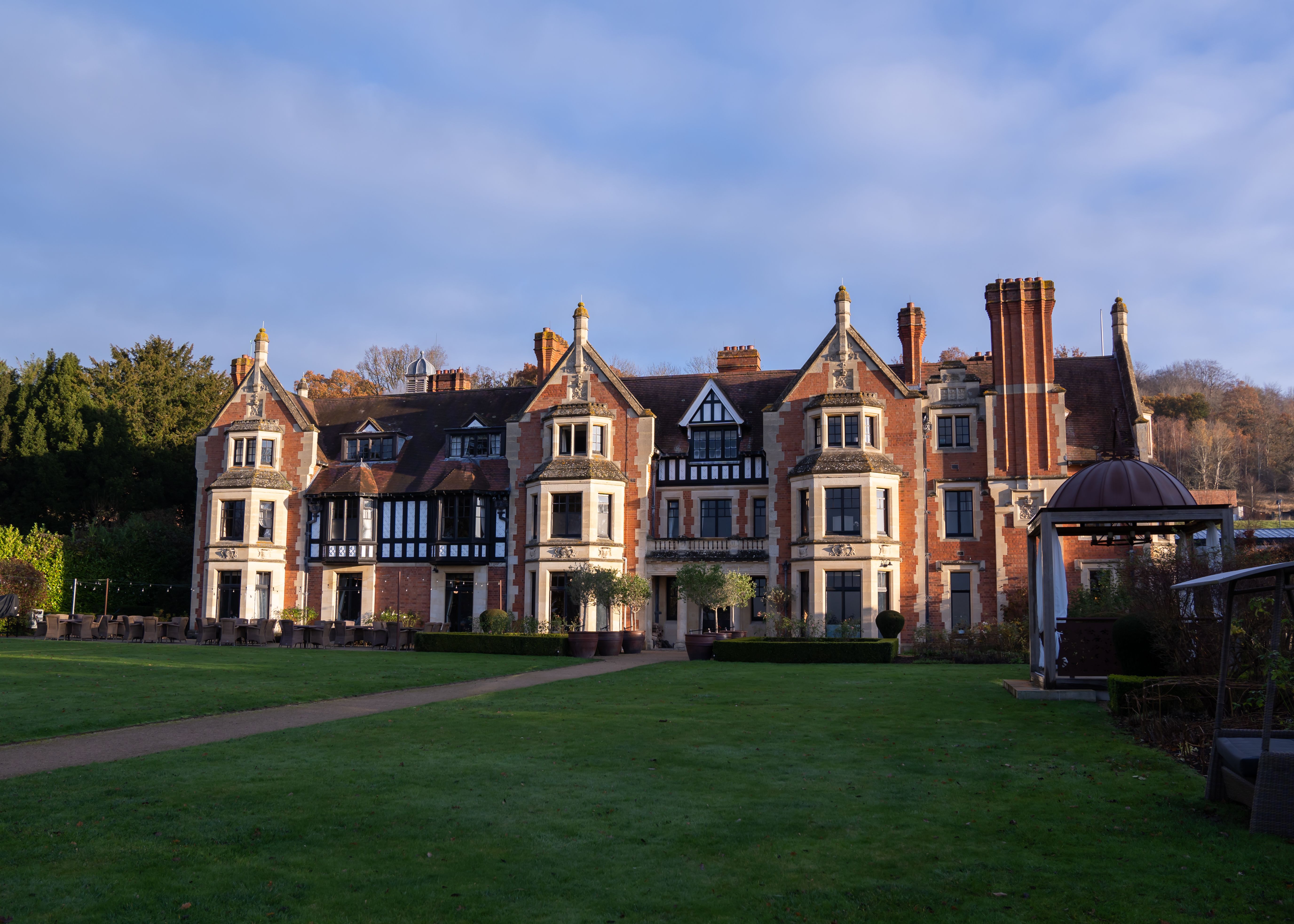 A large, historic manor house with multiple chimneys, brick and stone façade, and a well-kept lawn in front.