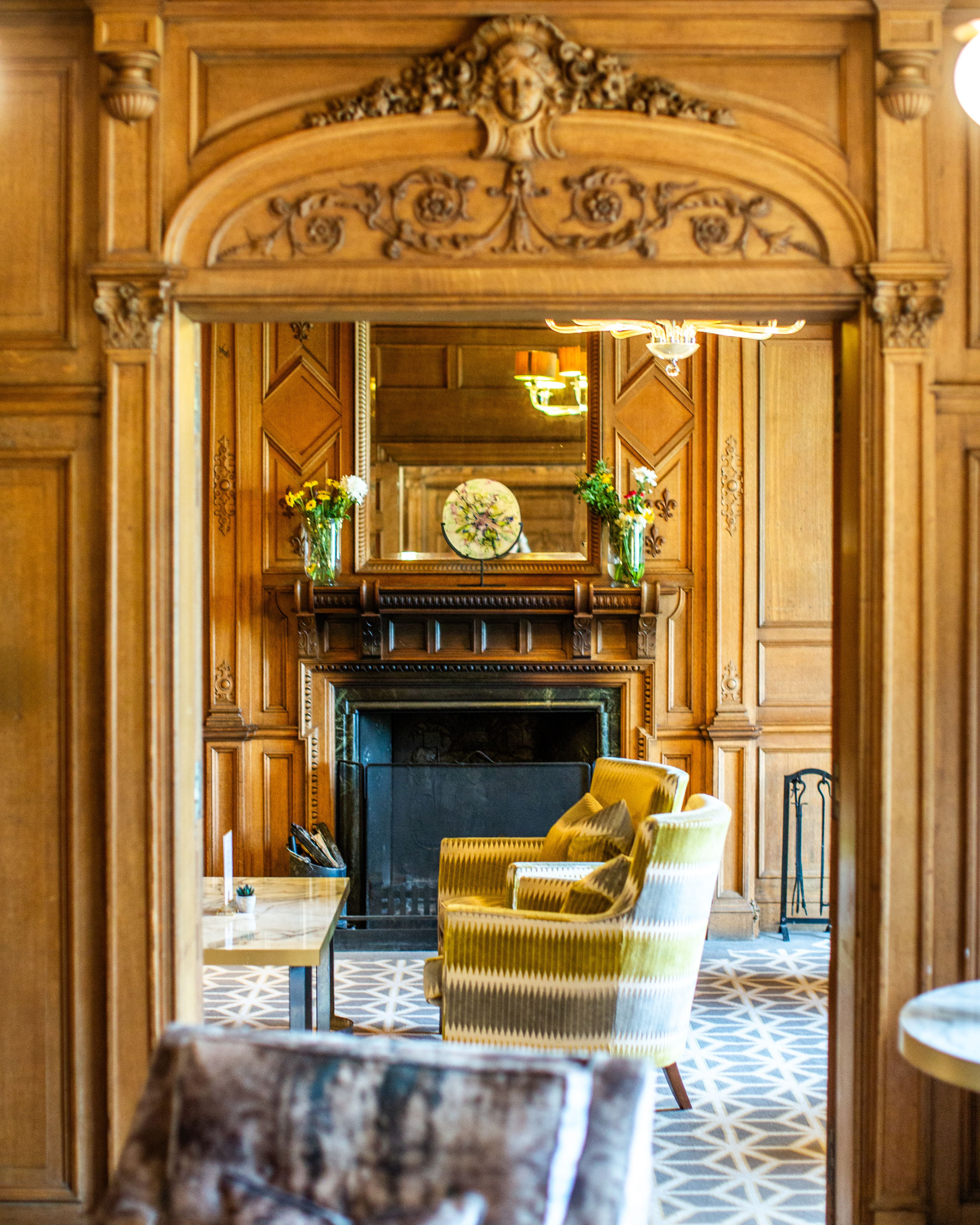 Elegant wooden-paneled sitting room with ornate fireplace, decorative archway, and upholstered armchairs