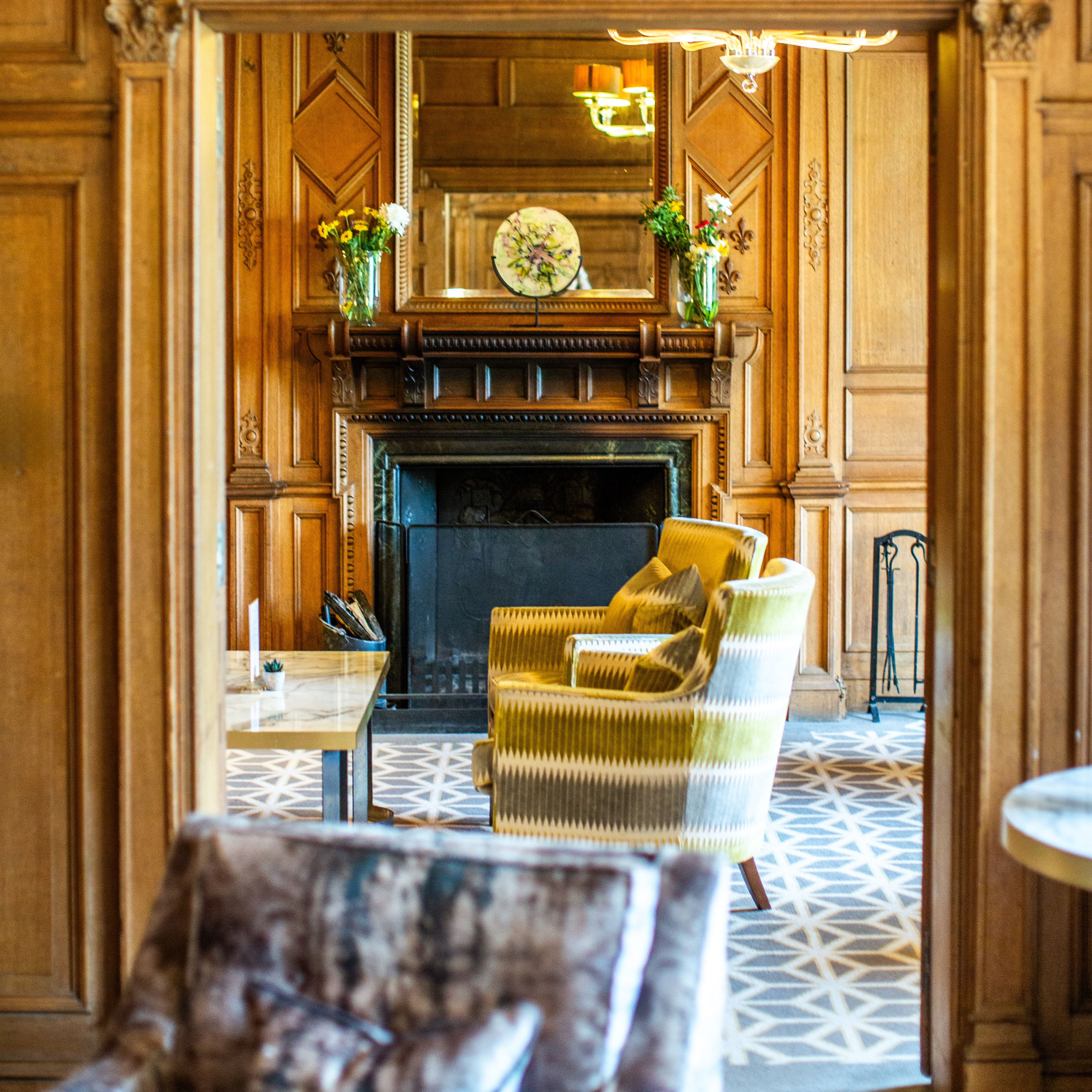 Elegant wooden-paneled sitting room with ornate fireplace, decorative archway, and upholstered armchairs