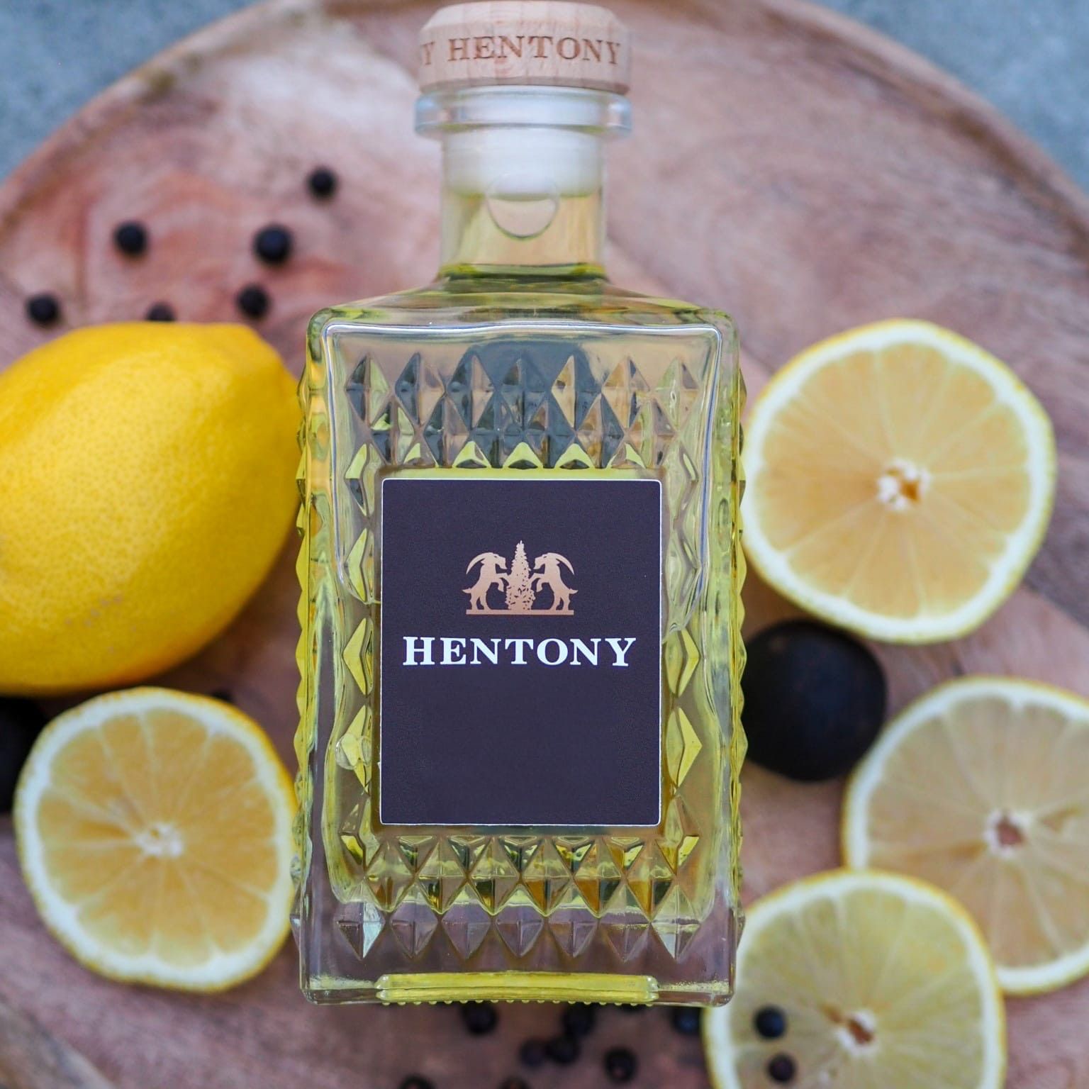 Hentony bottle with lemons and black peppercorns on a wooden tray