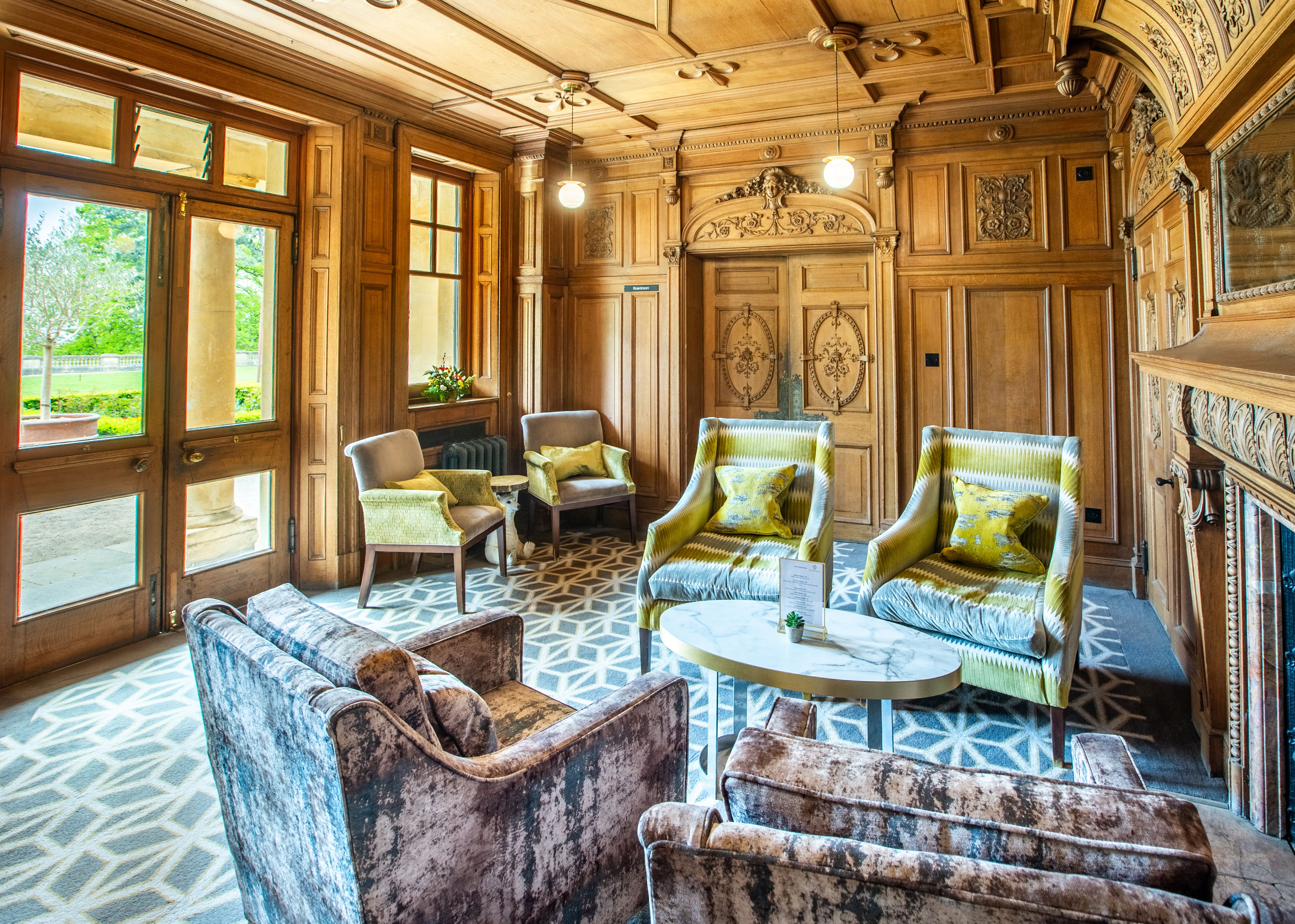 Elegant wood-paneled sitting room with velvet armchairs, ornate ceiling, and geometric carpet.