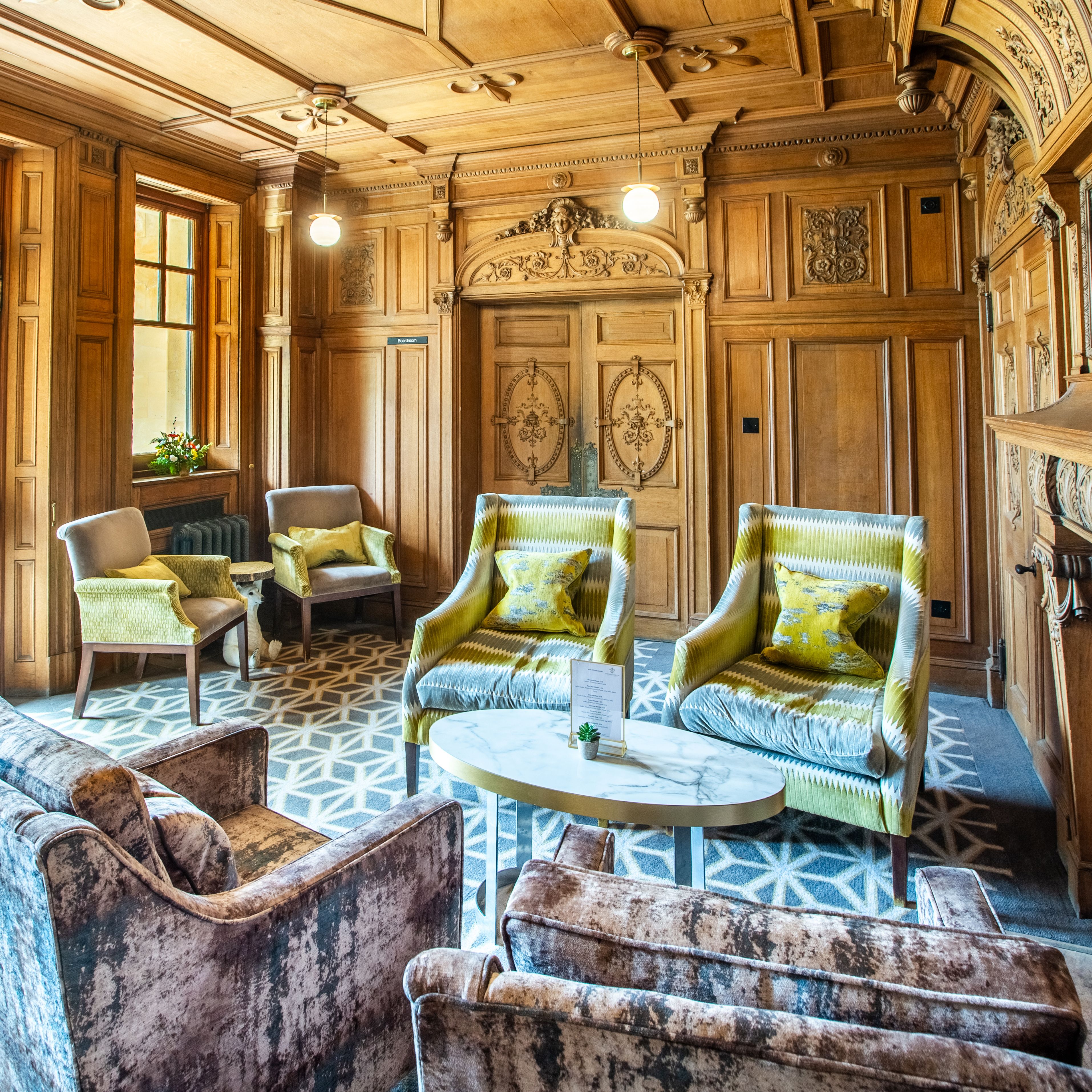 Elegant sitting room with wooden paneling, patterned carpet, armchairs, and a decorative fireplace