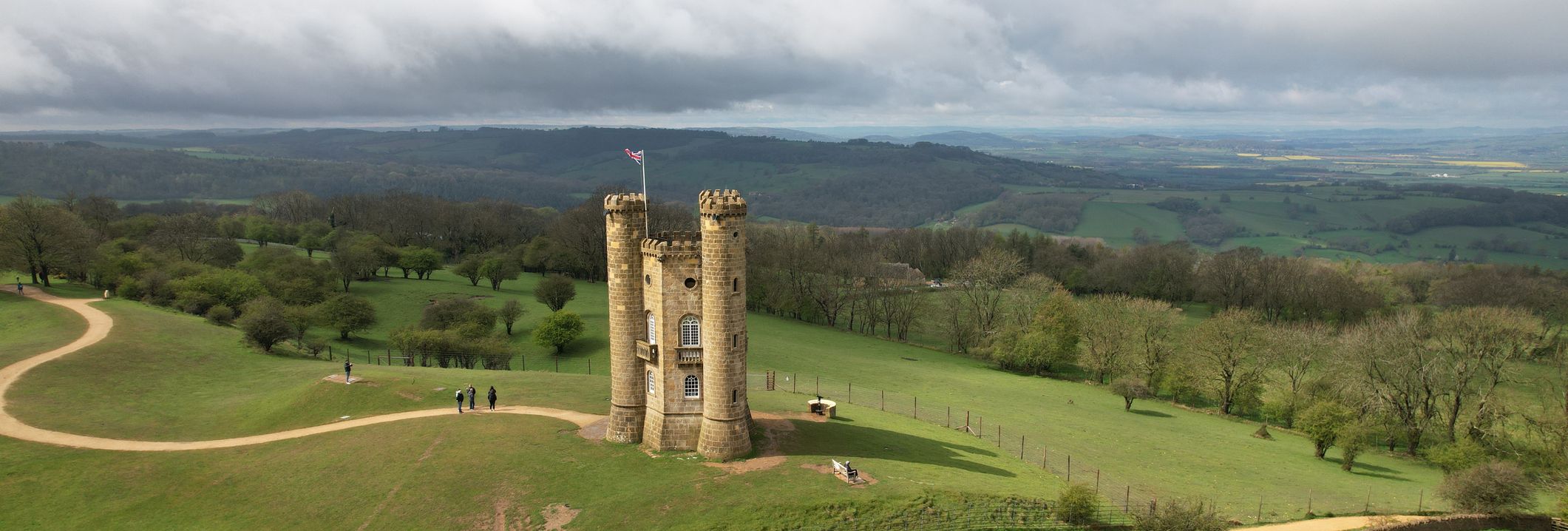 Aerial view of a small stone tower with three circular turrets on a hill surrounded by green fields and trees.