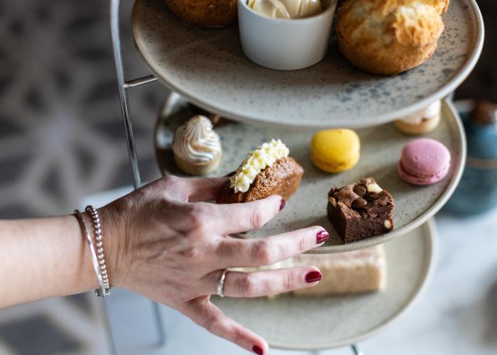 A hand reaching for a dessert from a tiered tray of assorted pastries