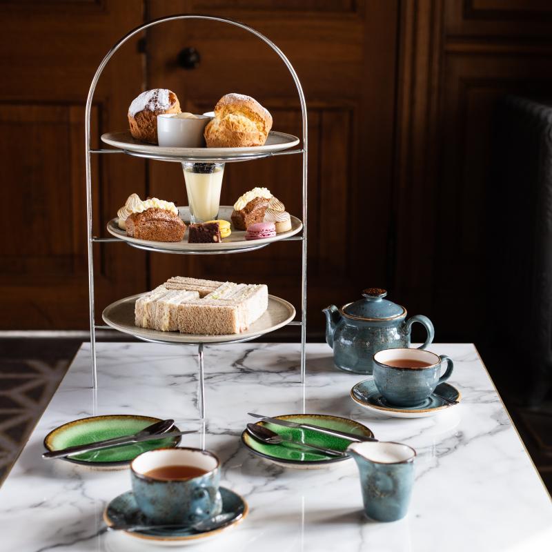 Afternoon tea stand with sandwiches, cakes and scones on a marble table with teapot and cups